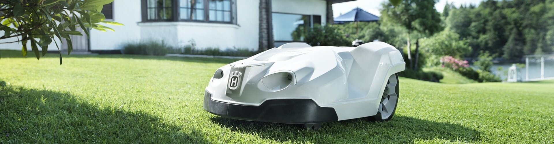 weißer Rasenmäher-Roboter fährt auf einer Wiese vor einem weißen Einfamilienhaus