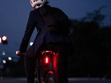 Intelligente Fahrrad-Gadgets: Was Radfahren sicherer macht Ein Fahrradfahrer bei Nacht. Zu sehen von hinten. Er Trägt einen Helm und ein rotes Licht ist m Fahrr