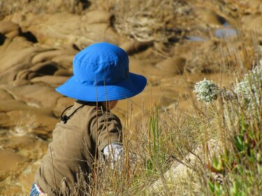 Ein Kind klettert mit einem UV-Hut durch eine wüstenähnliche Landschaft