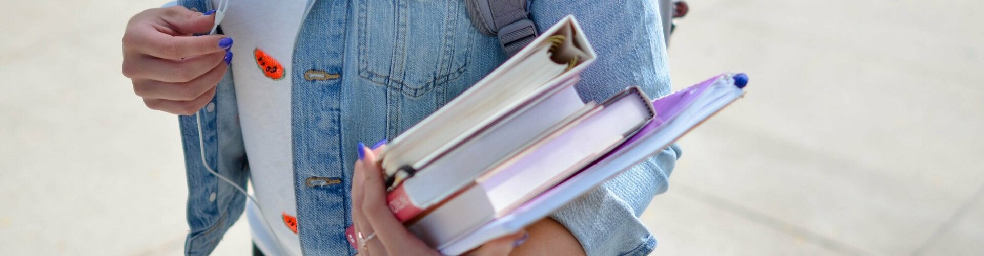 Mädchen in Jeansjacke mit Rucksack trägt vier Bücher 