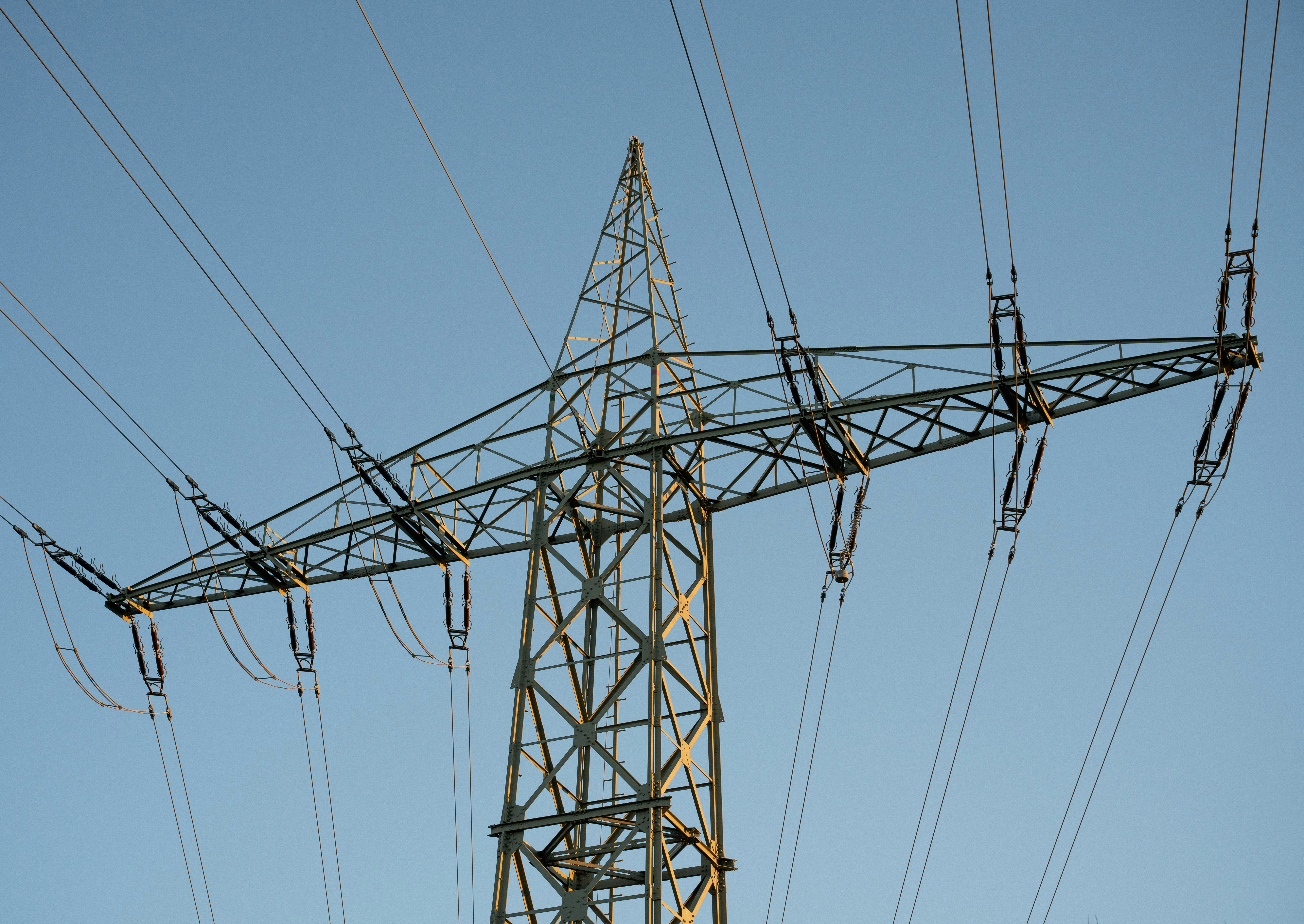 Ein hoher Strommast aus Stahlgitter gegen einen blauen Himmel.